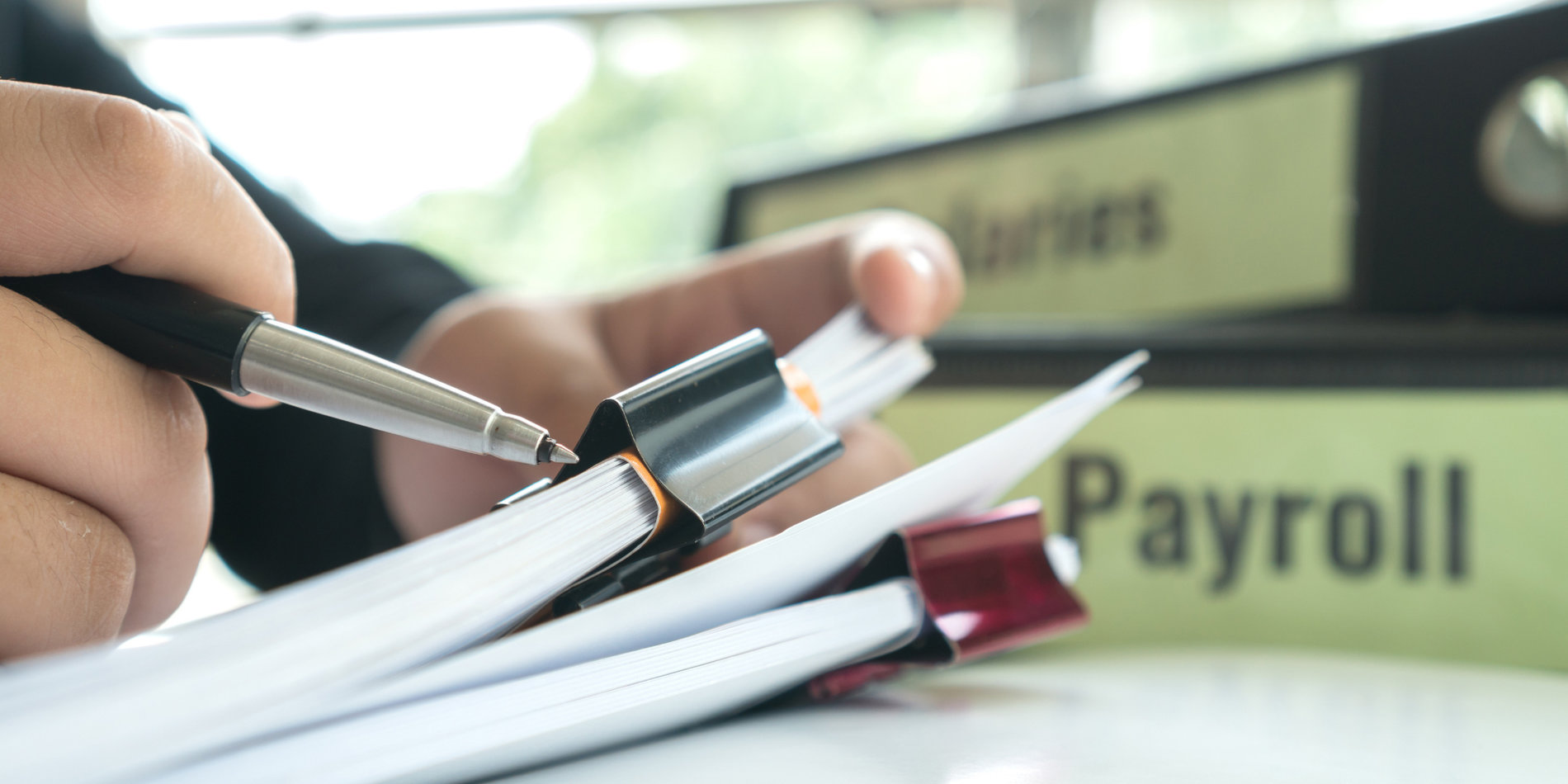Businessman manager hands holding pen for signing paperwork near payroll salary binder