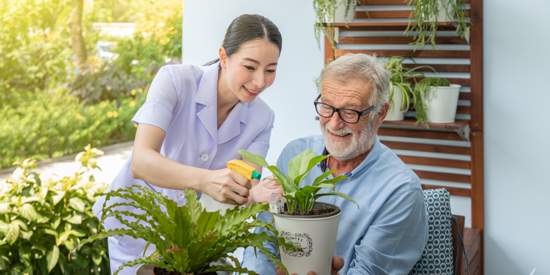 Caregiver assisting senior old man take care of small tree on table