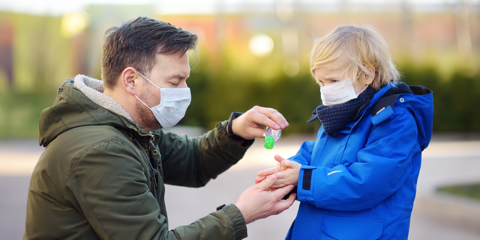 Mature man and little child wearing a protective mask and disinfecting their hands with sanitizer