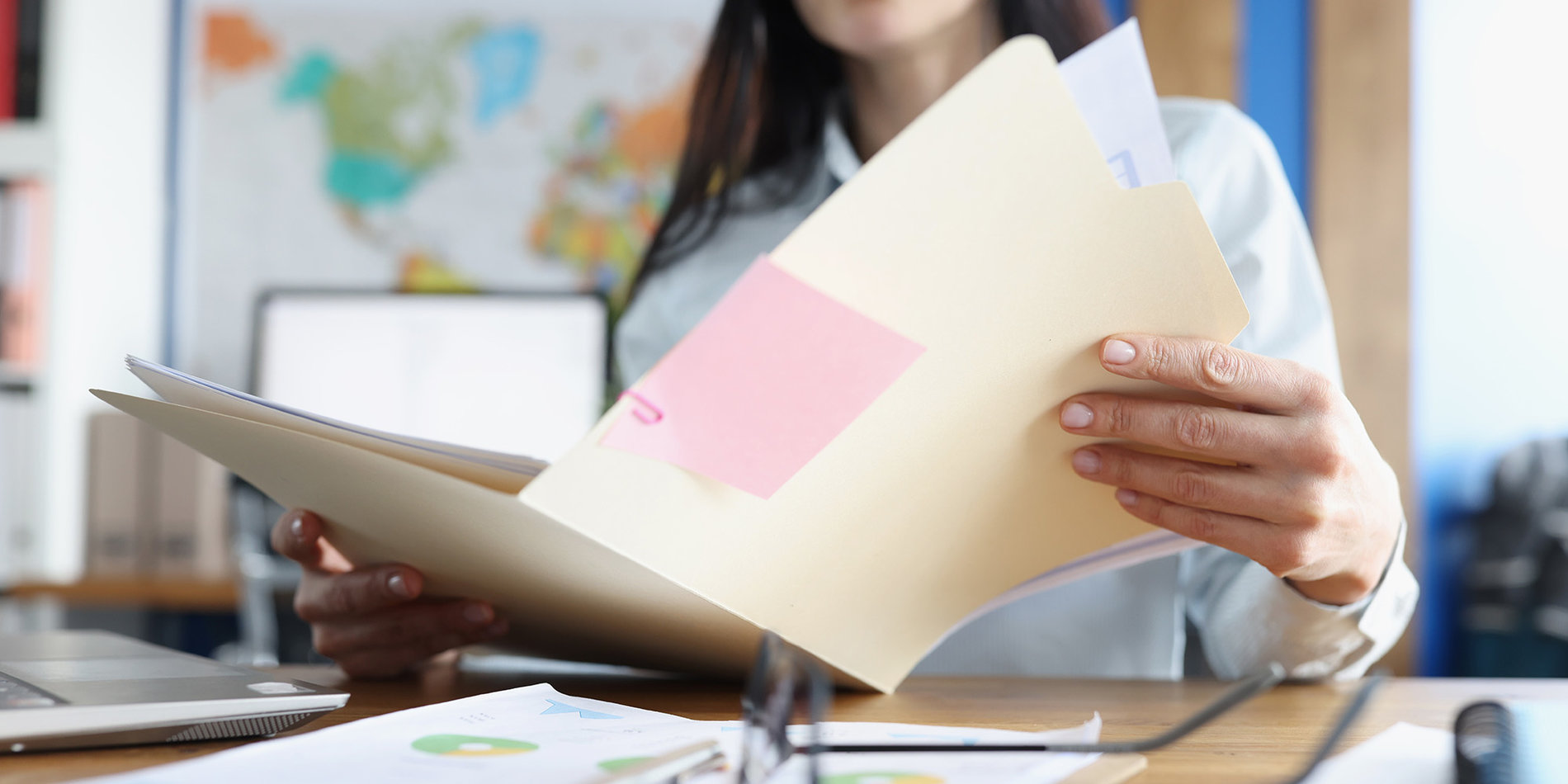 Female holding a manila file folder that has a pink post-it on the front