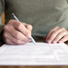 Man Writing on Paper with Pen on Table